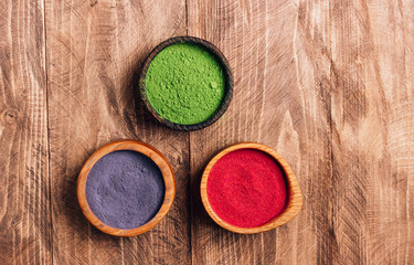 Obraz na płótnie Canvas Different colors of japanese matcha tea: green, red and blue in wooden bowls on wooden background. Acai berry powder, green tea leaf powder, and clitoria flower powder. Top view. Flat lay. Copy space
