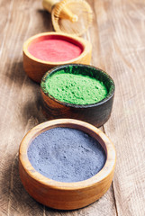 Fototapeta na wymiar Different colors of japanese matcha tea: green, red and blue in wooden bowls on wooden background. Acai berry powder, green tea leaf powder, and clitoria flower powder. Selective focus