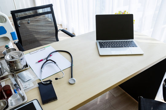 Laptop Computer With A Blank White Screen With Stethoscope,vial,syringe,empty Paper Clipboard And Medical Bottle Different Drugs On Surgical Tray With Medical Equipment On Wooden Table Background