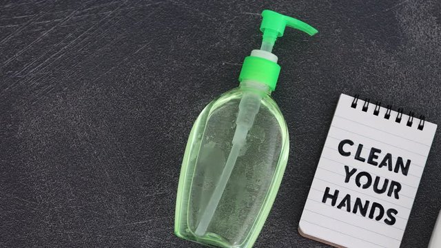 hand sanitizer and liquid soap next to memo with Clean your Hands text, flatlay version with camera panning horizontally