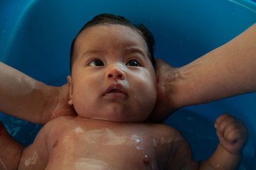 Mom holding her baby while bathing him in a tub full of water