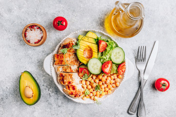 Healthy vegetable buddha bowl lunch with grilled chicken and chickpeas, cucumber, tomato and avocado on light gray background. Top view. Zero waste concept