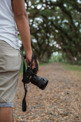 portrait of a man hand holding a camera taking picture of the road between large trees