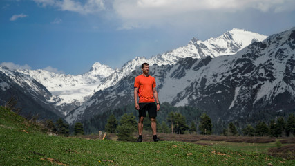 Naklejka premium The guy standing on a mountain with a green meadow sticking out veins on the hands and feet on the background of snow