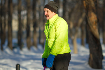 Senior mature man with black moustache wearing bright outfit making workout (pull- ups and flips) on a sports ground in the park on a sunny winter day