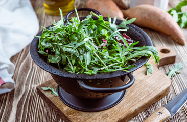 Fresh organic arugula leaves in black colander. Arugula or rucola for salad on wooden rustic background. Zero waste concept. Selective focus