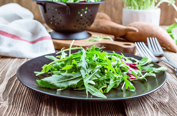 Fresh organic arugula leaves on black plate. Arugula or rucola for salad on wooden rustic background. Zero waste concept. Selective focus
