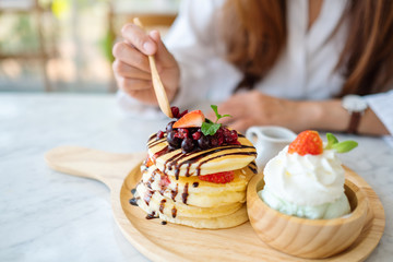 A woman eating a mixed berries pancakes with ice cream and whipped cream by wooden spoon