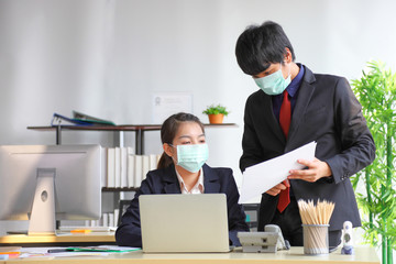 Manager and secretary are working in business office while wearing medical face mask for protecting and preventing the infection of corona virus or covid-19