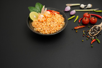 Instant noodles, spicy hot and spicy shrimp soup with Thai spices put on the table in the kitchen, black background