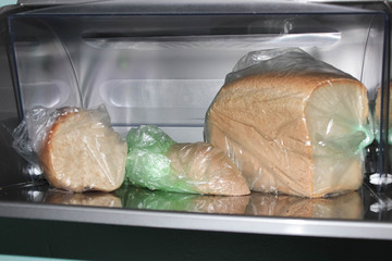 Different loaves of bread in a bread box and cellophane bags.