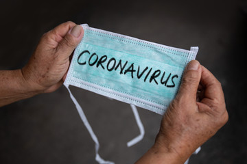 Old man holding a green medical face mask with CORONAVIRUS text on black background