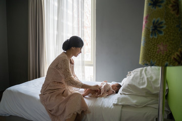Obraz premium Asian young mom wearing dress changes the baby's diaper in the bedroom when baby crying