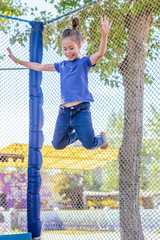 The child joyfully jumps on a big trampoline in the park.