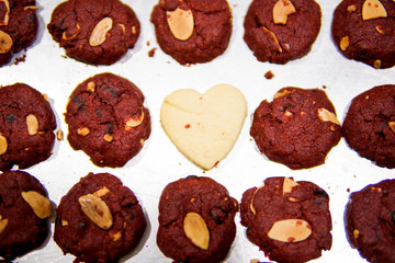 Love shape cookies in the middle of red velvet cookies on a tray