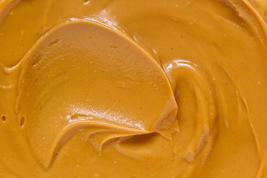 Peanut butter texture background. Brown nut paste smear closeup. Delicious natural food creamy smooth spread macro top view