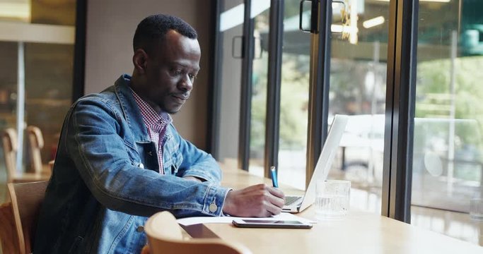 One young African businessman busy working in the office writing note on the book young black adult student study in cafe freelancer people working with laptop by the window 