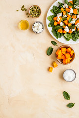 Salad with pumpkin and basil - near ingredients - on beige background top-down copy space