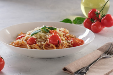 Spaghetti in tomato sauce with cherry tomatoes and basil on a white plate on a light background