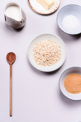 Ingredients for oat porridge: rolled oats or flakes, sugar, salt, milk and butter in a bowls on grey concrete background. Healthy eating, vegetarian food concept. Top view. Selective focus