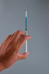 Hand holding vaccine with injection syringe isolated on gray background.