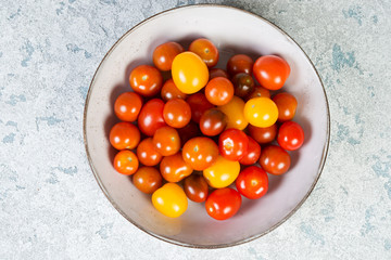 Lots of little colored cherry tomatoes in a plate. Close- up, top view.