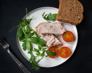 Appetizer with sliced ham, chopped cherry tomatoes and fresh arugula on a light plate