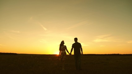 Fototapeta na wymiar beautiful girl and guy go hand in hand in rays of sun in spring. happy married couple. happy family concept. young couple in love walks and listens to music on a smartphone.