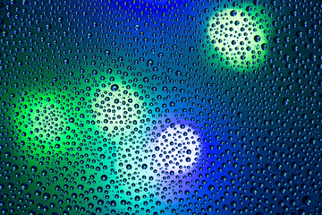Closeup photo of shiny small circles of water drops on wet dark blue window with city lights