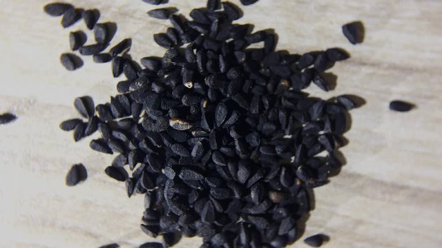 Nigella seeds or Black cumin or Black onion seed, and Black sesame seed in dish with male hand on wooden
