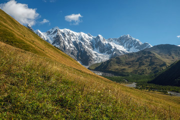 Blue clear sky sunny day big mountains with snow green slope with grass Svaneti Georgia