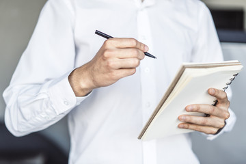 Man writes standing with a pen in notebook in a sunny office, business and education concept. Close up