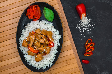 Chinese dish on stone background. Chicken with rice in black plate on wooden board. Horizontal shot.