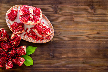 Juicy pomegranate with seeds on plate on dark wooden table top-down copy space