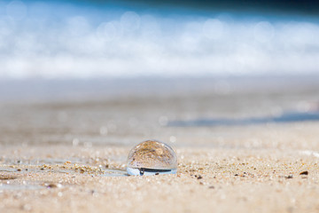 初夏の海の砂浜で遊んでいる子供姉妹と透明な水晶ガラスボール