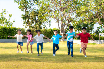 Large group of happy Asian smiling kindergarten kids friends holding hands playing and running in the park on sunny summer day in casual clothes..