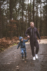 A little boy walks in the woods with his dad wearing walking jumpsuits