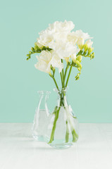 Fragrance soft light white flowers freesia in bouquet in glass vases in green mint menthe interior on white wood board.
