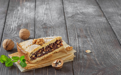 Slice of homemade hazelnut cake on a dark vintage wooden background. Near walnuts and a sprig of mint. Close-up Copy Space