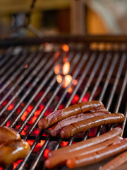 Appetizing delicious sausages lie on the grill of a roasting pan in the dark. From underneath the grill, hot coals burn. Outdoor festive refreshments in the city.