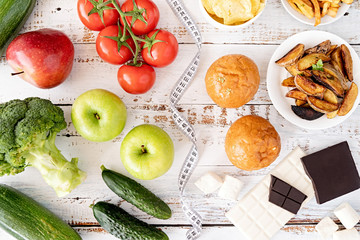 Healthy and unhealthy food concept. Fruit and vegetables vs sweets and potatoe fries top view flat lay on wooden background