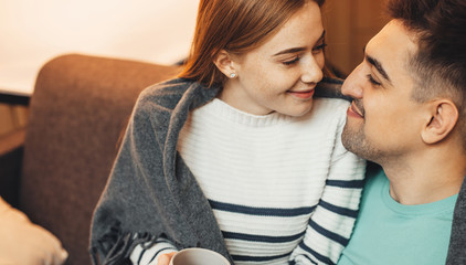 Cheerful caucasian couple embracing each other while sitting on the sofa during a sunny weekend day