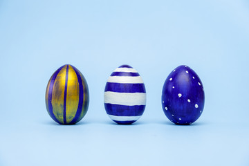 Three easter trendy colored classic blue and golden decorated eggs striped pattern on blue. Happy Easter card with copy space for text. Minimal style.