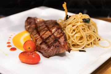 Medium grilled striploin beef steak with spaghetti olio a side dish served on white dish.