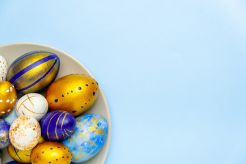 Happy Easter. Plate with easter eggs trendy colored classic blue, white and golden on blue background. Copy space. Minimal style. Flat lay, top view.
