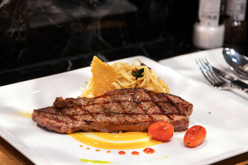 Medium grilled striploin beef steak with spaghetti olio a side dish served on white dish.