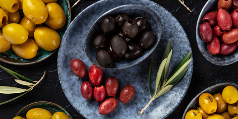 Olives overhead panorama. An assortment of green, black and red olives, shot from the top on a dark table