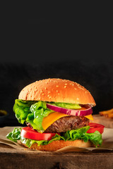 Burger with beef, cheese, onion, tomato, and green salad, a side view on a dark background with copy space