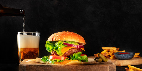 Burger and beer panorama. Hamburger with beef, cheese, onion, tomato, and green salad, a side view...