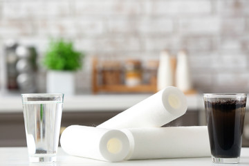 Glasses of clean and dirty water with filters on table in kitchen